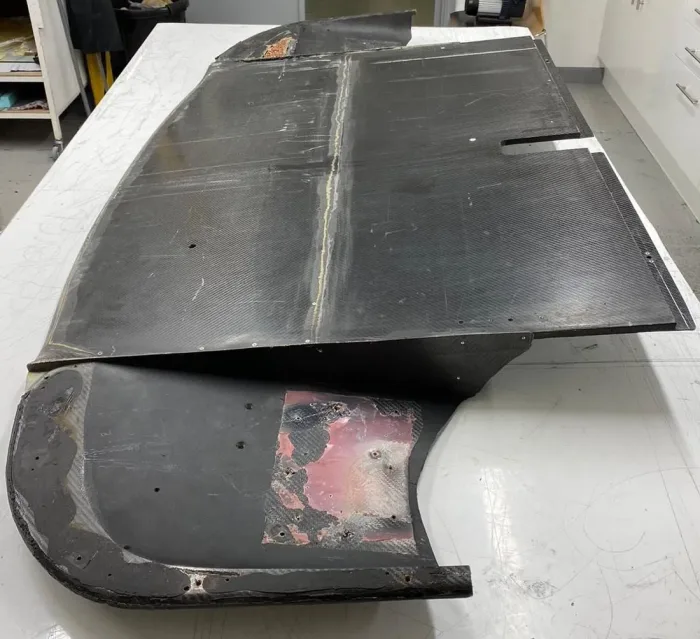 Underside of a damaged carbon fibre clamshell on the bench, filler visible before repair